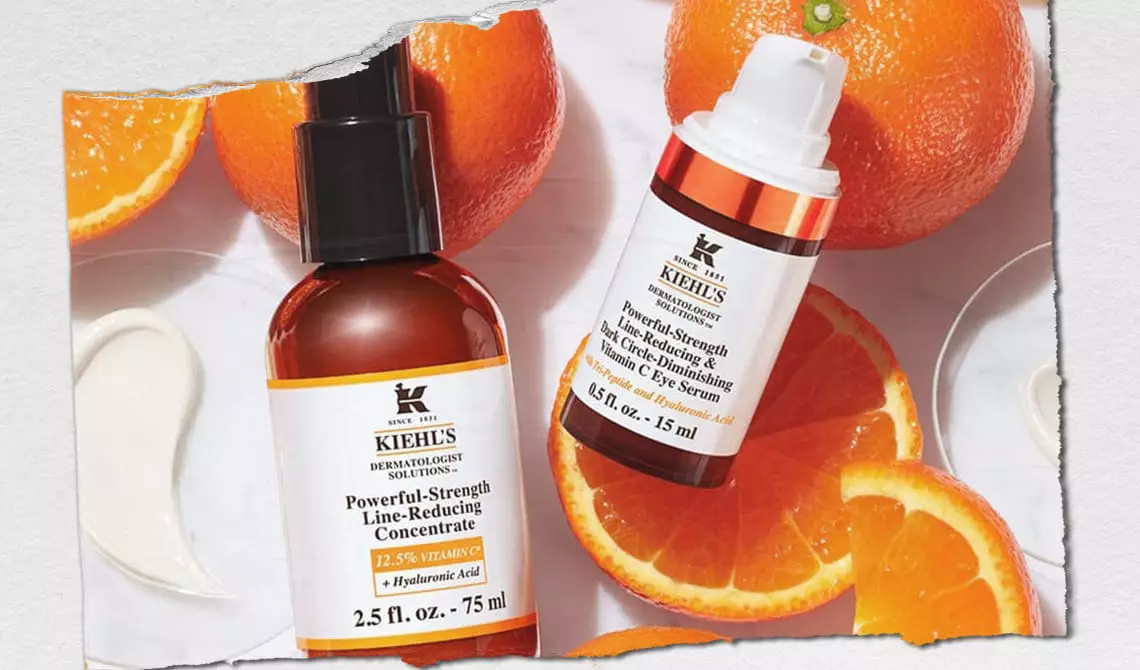 Bottles of Kiehl’s formulas containing Vitamin C with oranges and orange slices in the background