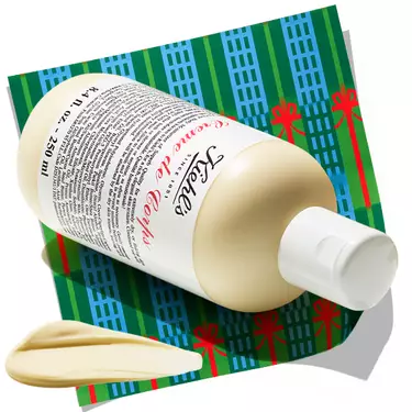 Bottle of Kiehl's Creme de Corps body lotion with a dollop of cream, resting on a patterned holiday background.