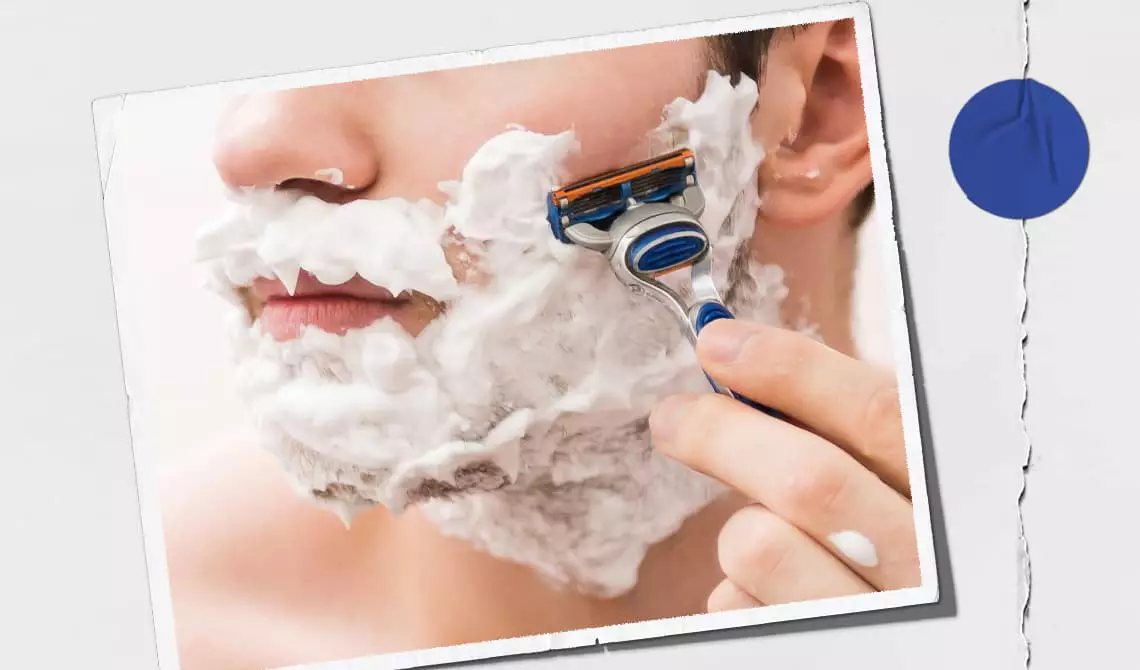 Model with shaving cream on their face shaving their cheek