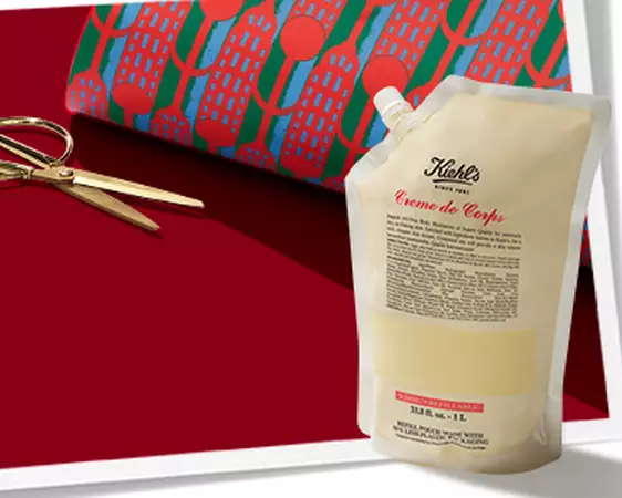 Kiehl's promotional banner featuring a body lotion refill pouch and gold scissors against a red background. 