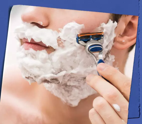 Model with shaving cream on their face shaving their cheek